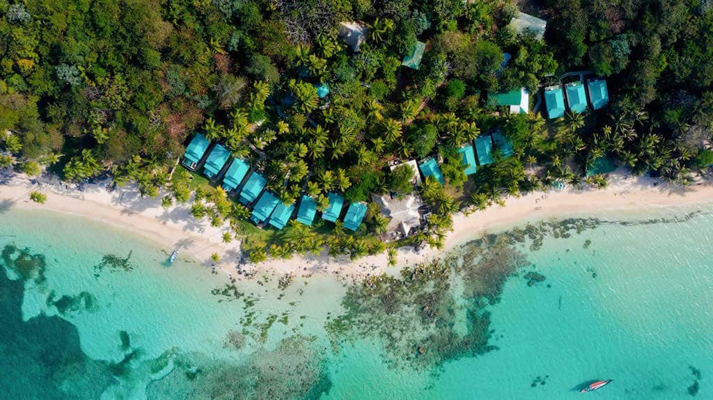 A drone view of tropical Caribbean island with emerald waters, white sand beach and lots of palm trees with blue villas in the palm trees in Little corn island in Nicaragua at Yemaya